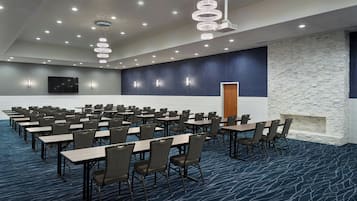 A conference room with rows of tables and chairs, a stone accent wall, and a large screen.