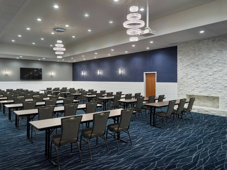 A conference room with rows of tables and chairs, a stone accent wall, and a large screen.