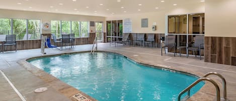 A swimming pool with a slide, seating area, and a view of trees through large windows.