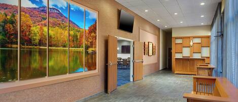 A hotel lobby with a large window displaying a scenic autumn landscape, a flat-screen TV mounted on the wall, and a reception desk area.