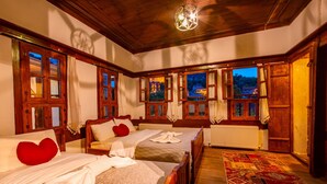 A room with two wooden beds, a large window with curtains, a patterned rug, and a ceiling light fixture. - Beyzade Konak Otel (Safranbolu)