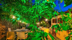 An outdoor dining area with tables and chairs, surrounded by lush greenery and a stone wall. - Beyzade Konak Otel (Safranbolu)