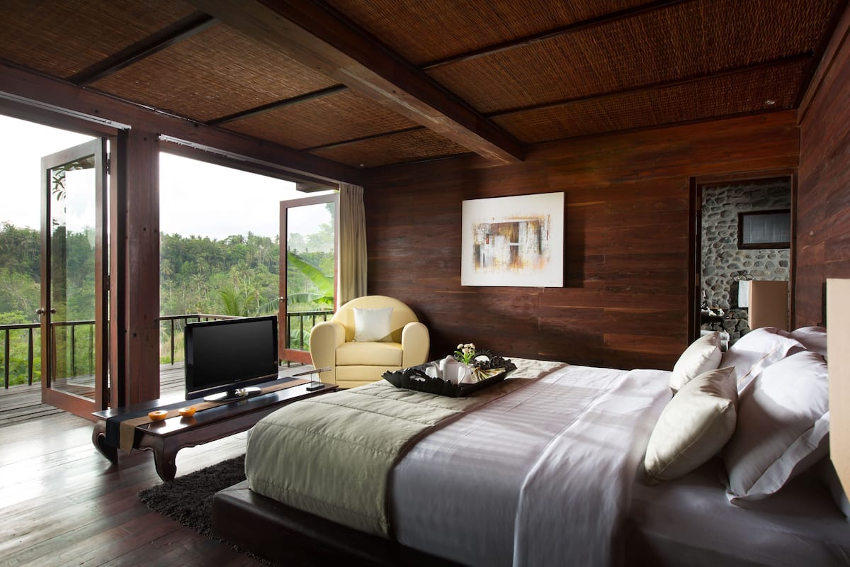A bedroom with a large bed, a television, a chair, and a view of the outdoors.