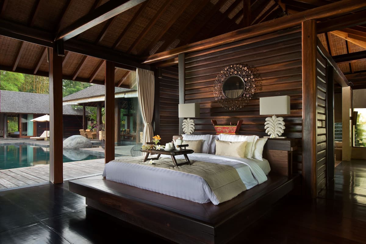 A spacious bedroom with a large bed, a wooden headboard, and a view of a swimming pool.