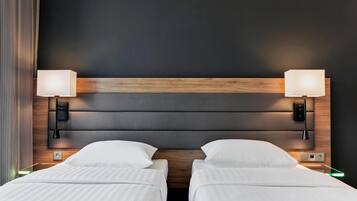 A hotel room with two beds, a wooden headboard, bedside lamps, and a nightstand with a lamp.