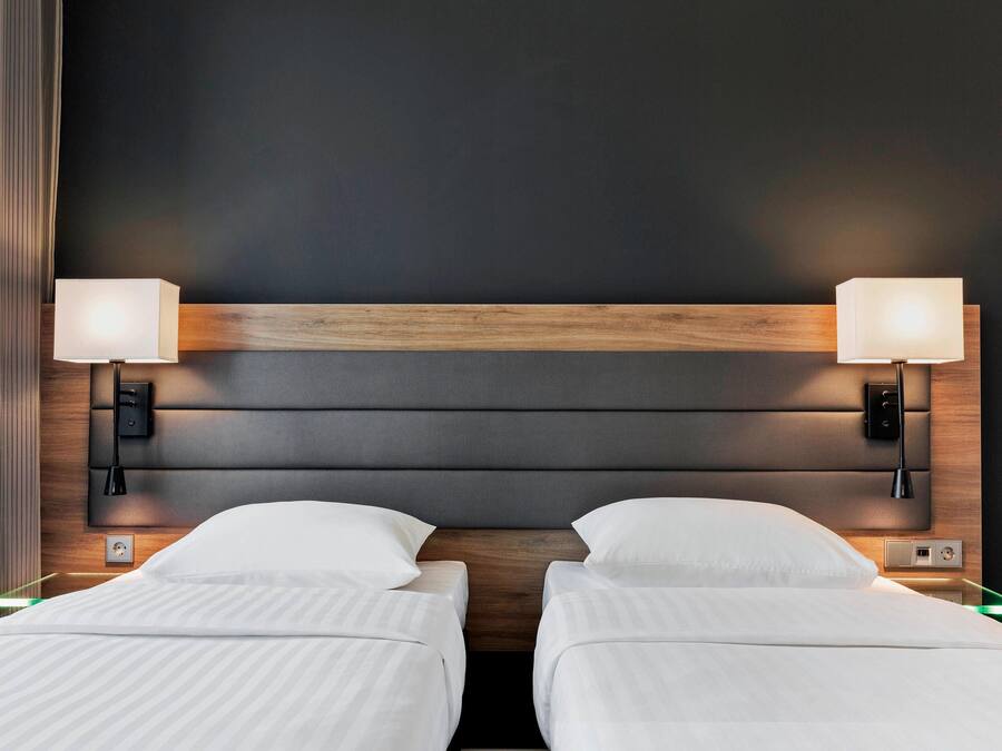 A hotel room with two beds, a wooden headboard, bedside lamps, and a nightstand with a lamp.
