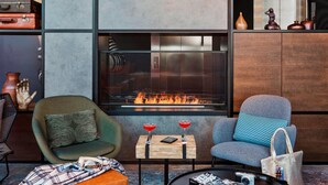 A modern lounge area with a fireplace, two armchairs, a small table with drinks, and a coffee table with a camera and a magazine.