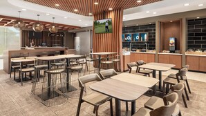 Un restaurant moderne avec un plafond en lambris de bois, de nombreuses tables et chaises, un comptoir doté d’un écran de télévision et un mur en briques avec des étagères.