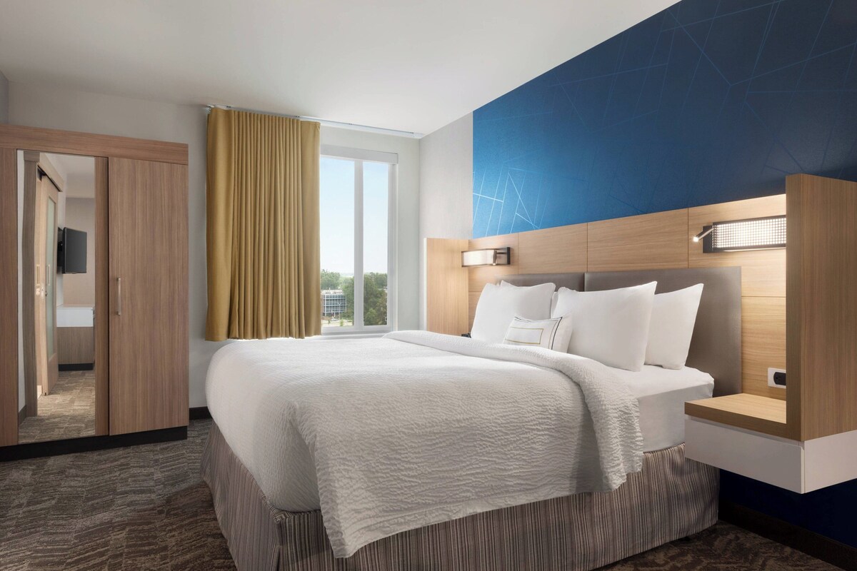 Una habitación de hotel con una cama grande, un armario de madera, un espejo y una ventana con cortinas.