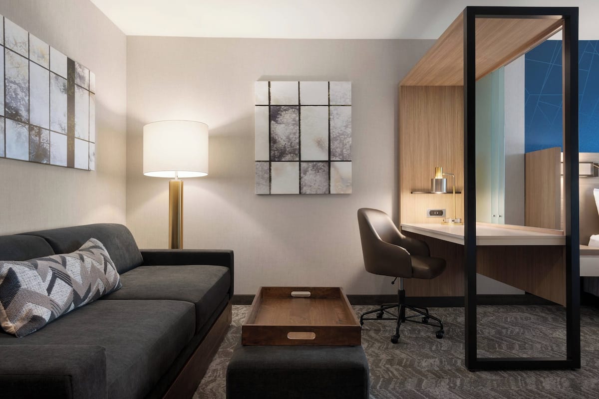 A modern hotel room with a sofa, a desk, a lamp, and artwork on the walls.