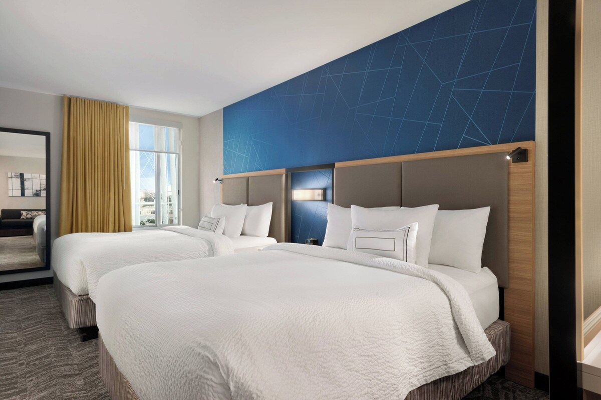 Habitación de hotel con dos camas, un espejo grande y vista a la ciudad.
