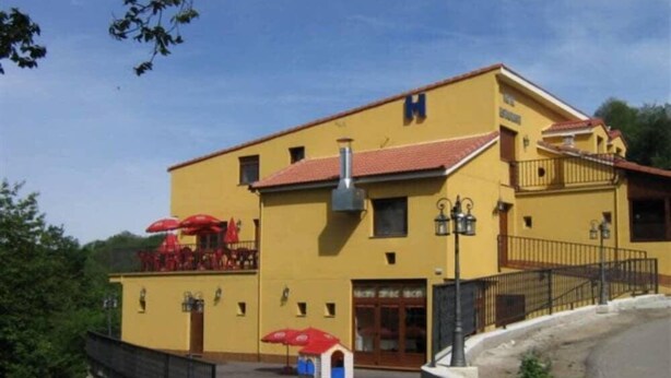 A yellow building with a red roof, a balcony, and outdoor seating with red umbrellas. - Hotel Rural Casa Migio (Mieres)