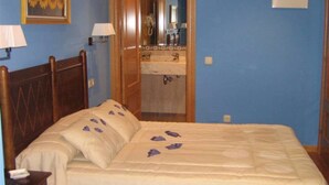 A bedroom with a wooden bed, a nightstand, a bedside lamp, a framed picture on the wall, and a bathroom visible through an open door. - Hotel Rural Casa Migio (Mieres)