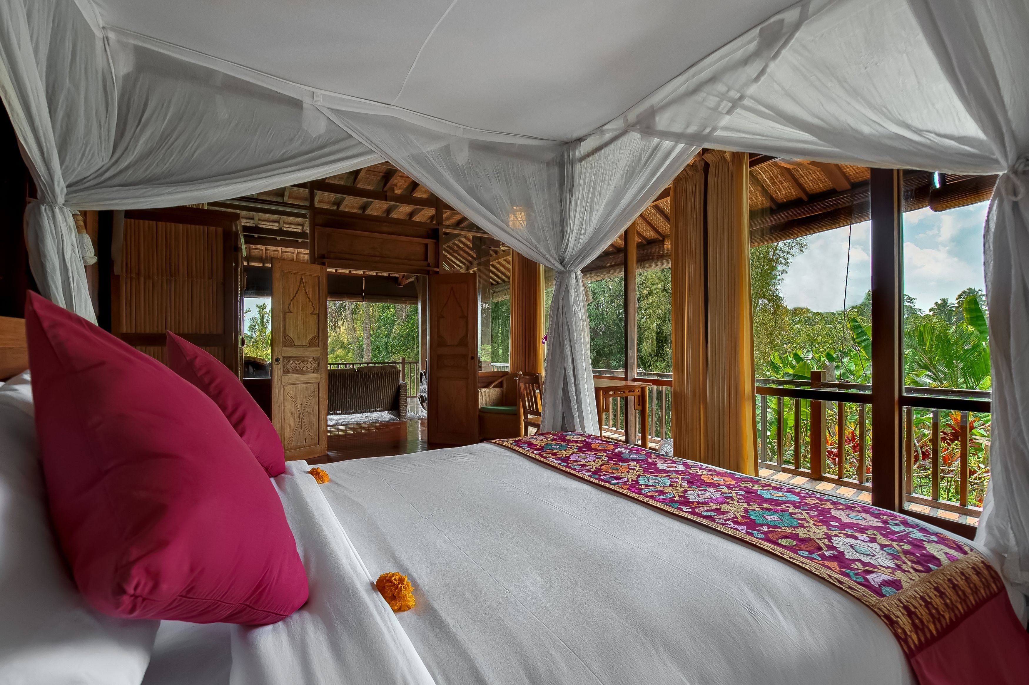 Ein Schlafzimmer mit Baldachinbett, einer Holzterrasse und Blick ins Grüne.