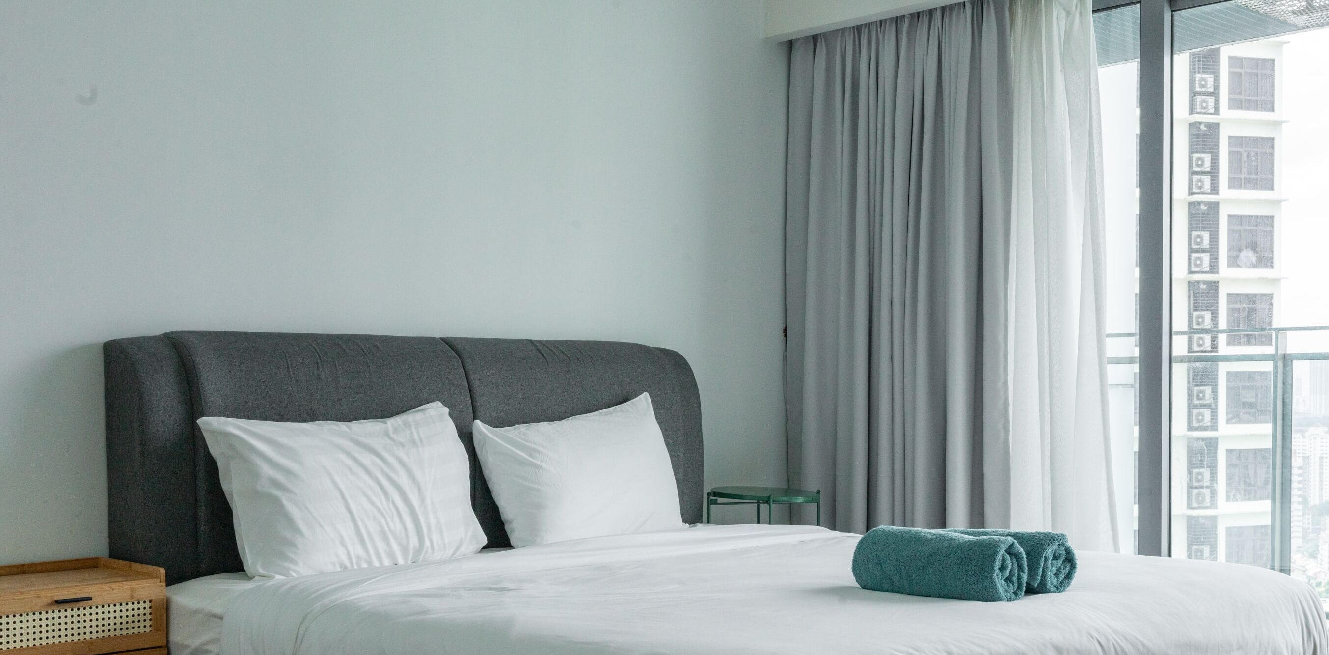 A hotel room with a large bed, grey headboard, white pillows, and a teal towel.