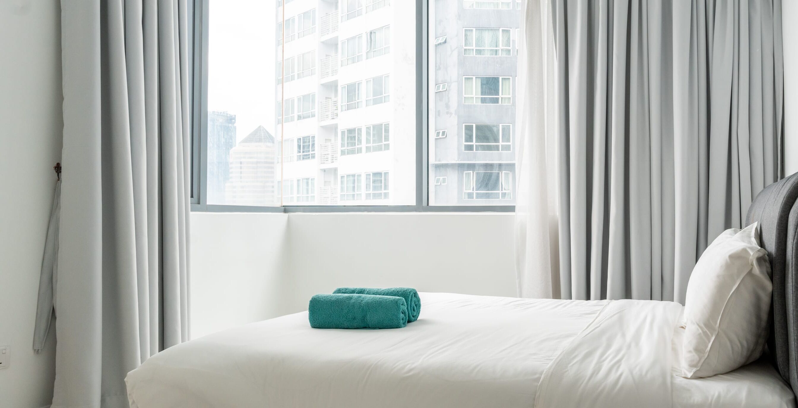 A hotel room with a bed, white curtains, and a view of a building through the window.