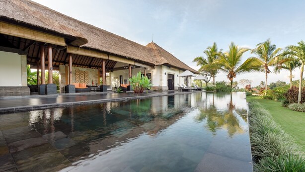 A pool area with a thatched-roof structure, palm trees, and a well-maintained lawn. - Villa Rumah Lotus (Payangan)