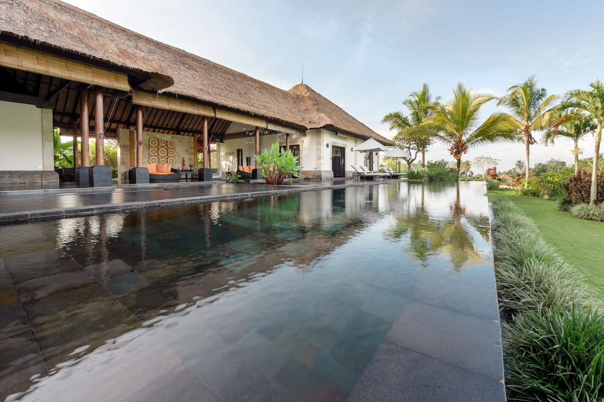 A pool area with a thatched-roof structure, palm trees, and a well-maintained lawn.
