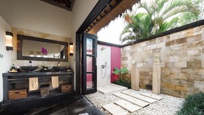 A modern bathroom with a large mirror, two sinks, a shower, and a stone wall. - Villa Rumah Lotus (Payangan)