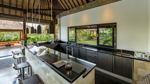 A modern kitchen with a large island, bar stools, and a view of the garden. - Villa Rumah Lotus (Payangan)