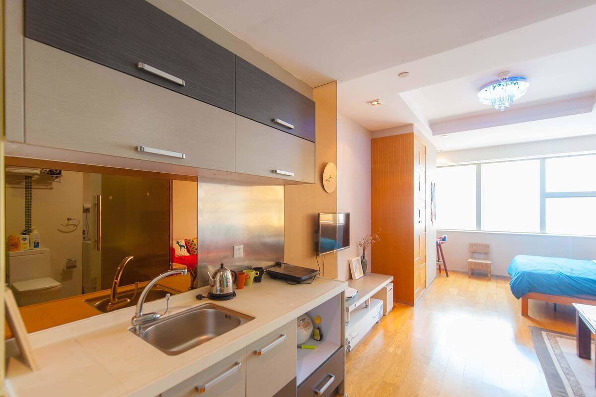 A modern kitchen with a sink, stove, and cabinets, a dining area with a table and chairs, and a large window providing natural light.