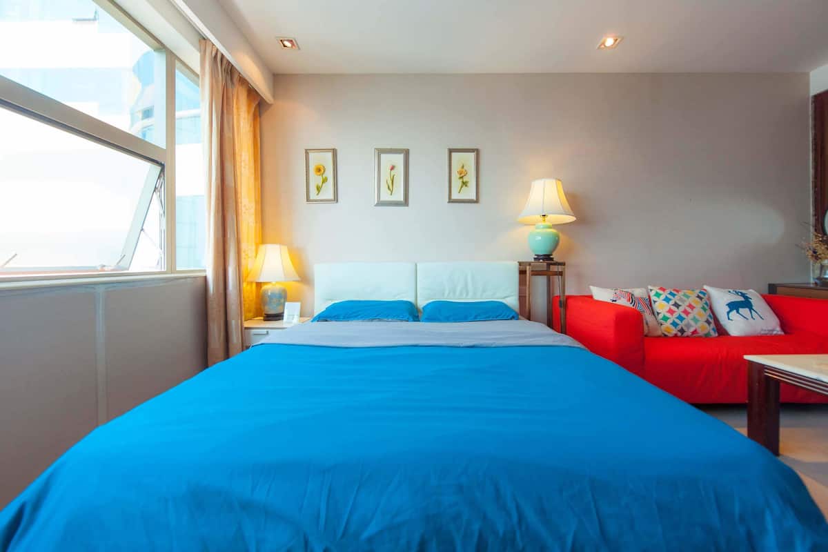 A hotel room with a large bed, a red sofa, and a window with curtains. There are three framed pictures on the wall and two lamps on the side tables.