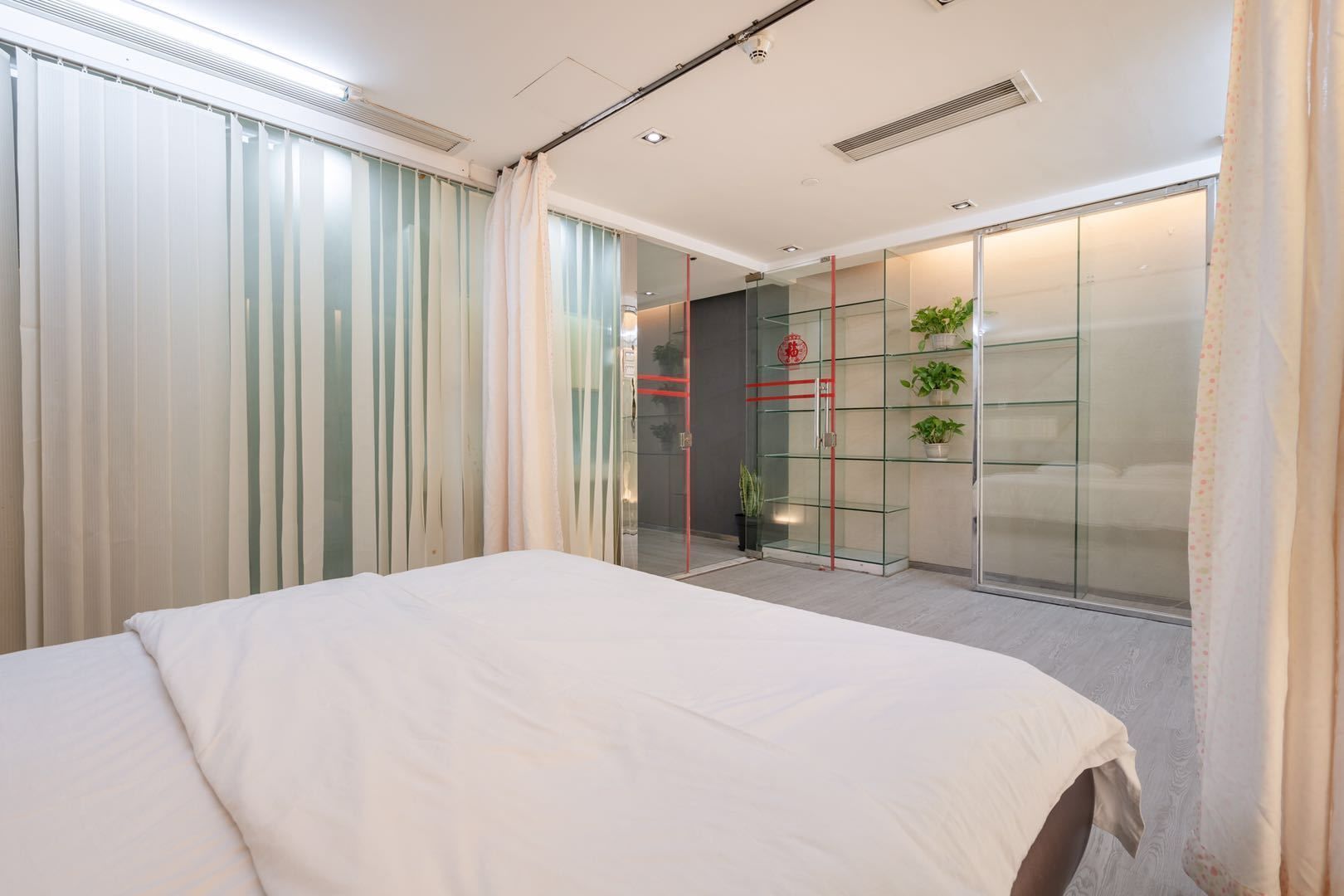 Una habitación de hotel moderna con una cama grande, un muro divisor de vidrio y una pequeña planta en una repisa.