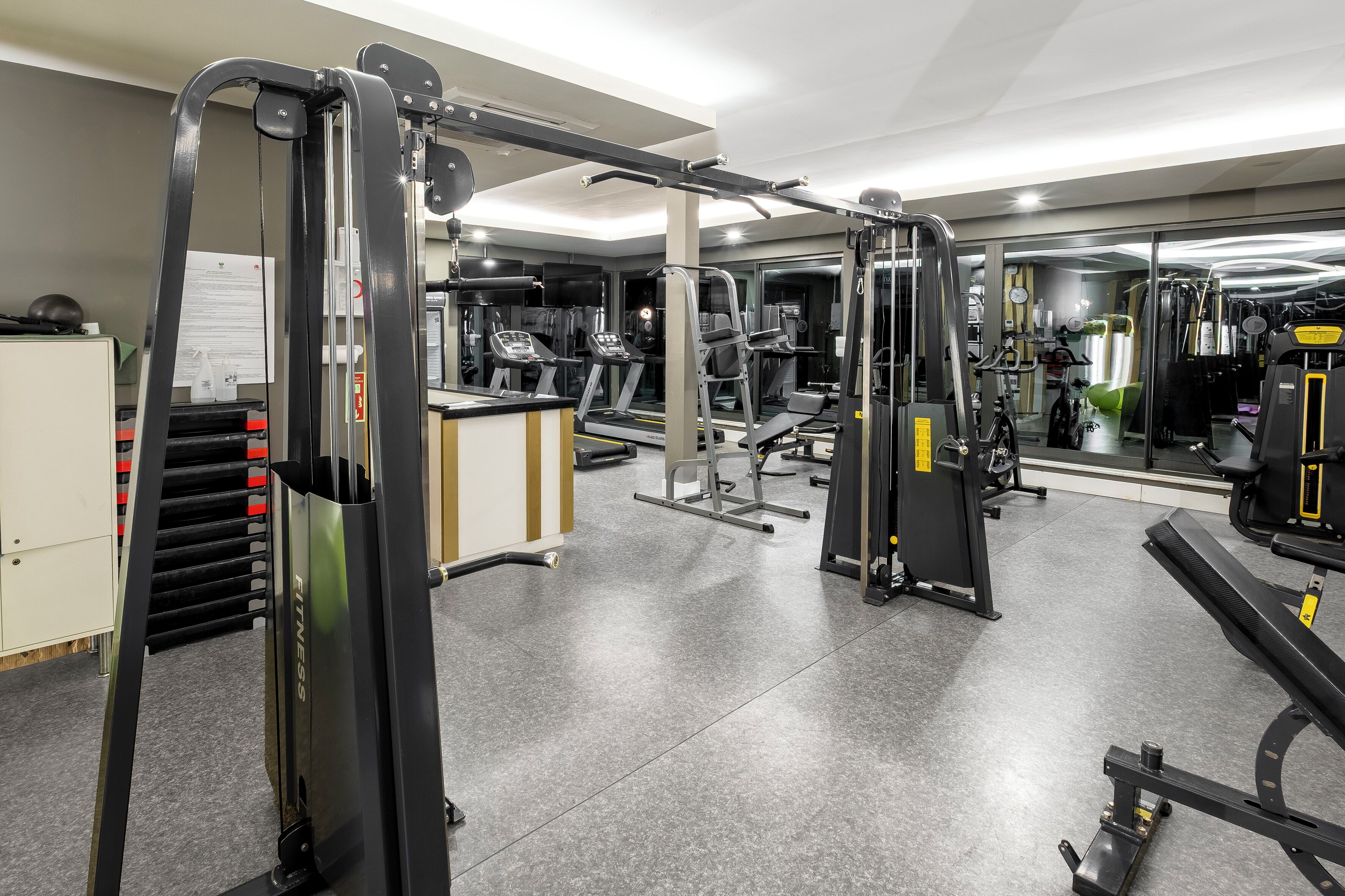 Une salle de sport équipée de divers appareils d’exercice, dotée d’un mur recouvert de miroirs et d’un tableau blanc sur lequel sont inscrites des instructions.