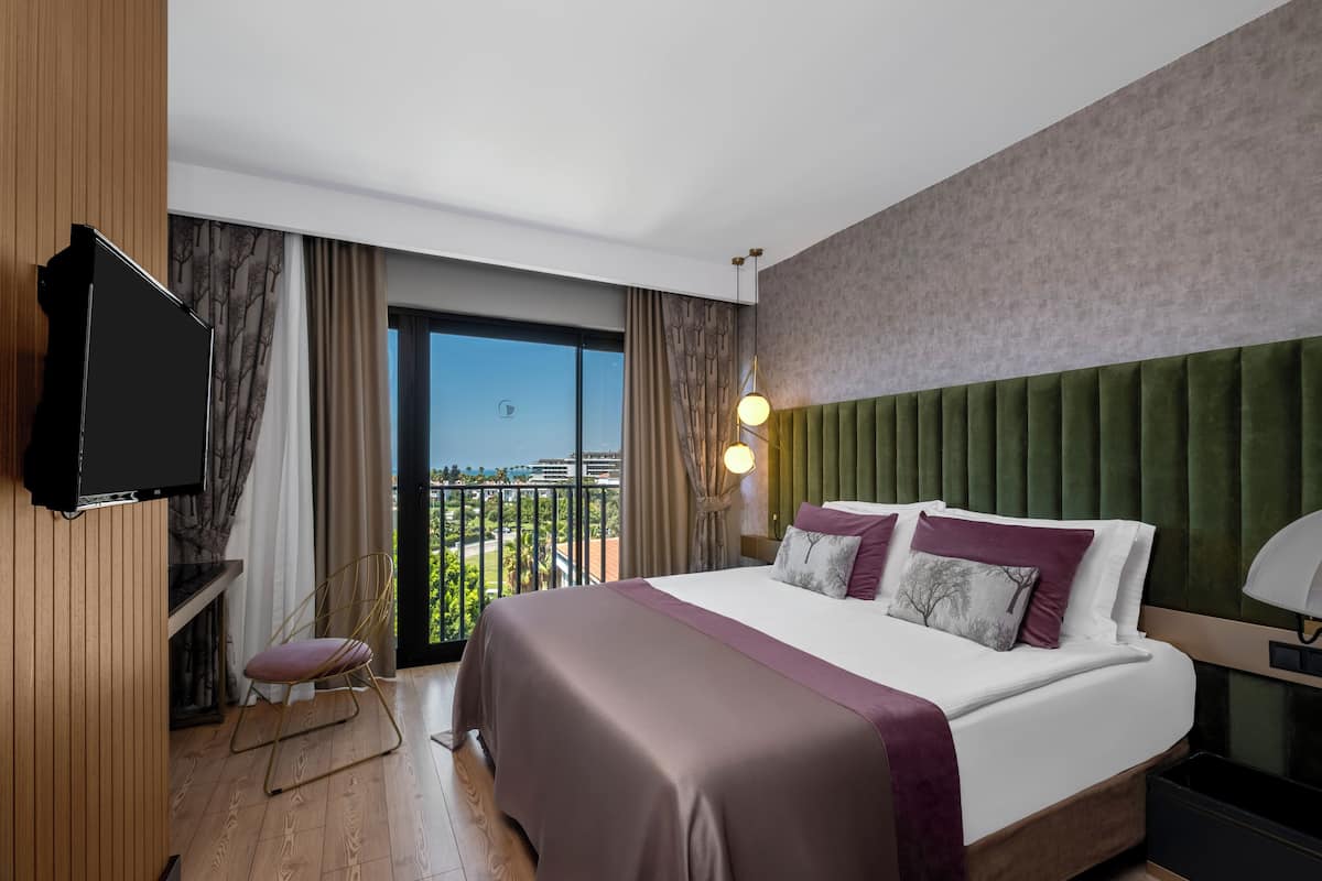 Una habitación de hotel moderna con una cama grande, un televisor, un balcón con vistas y un cabecero verde.