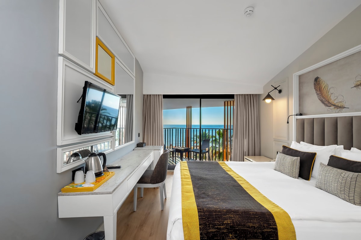 Habitación de hotel con cama, escritorio con televisor, cafetera y vista al mar.