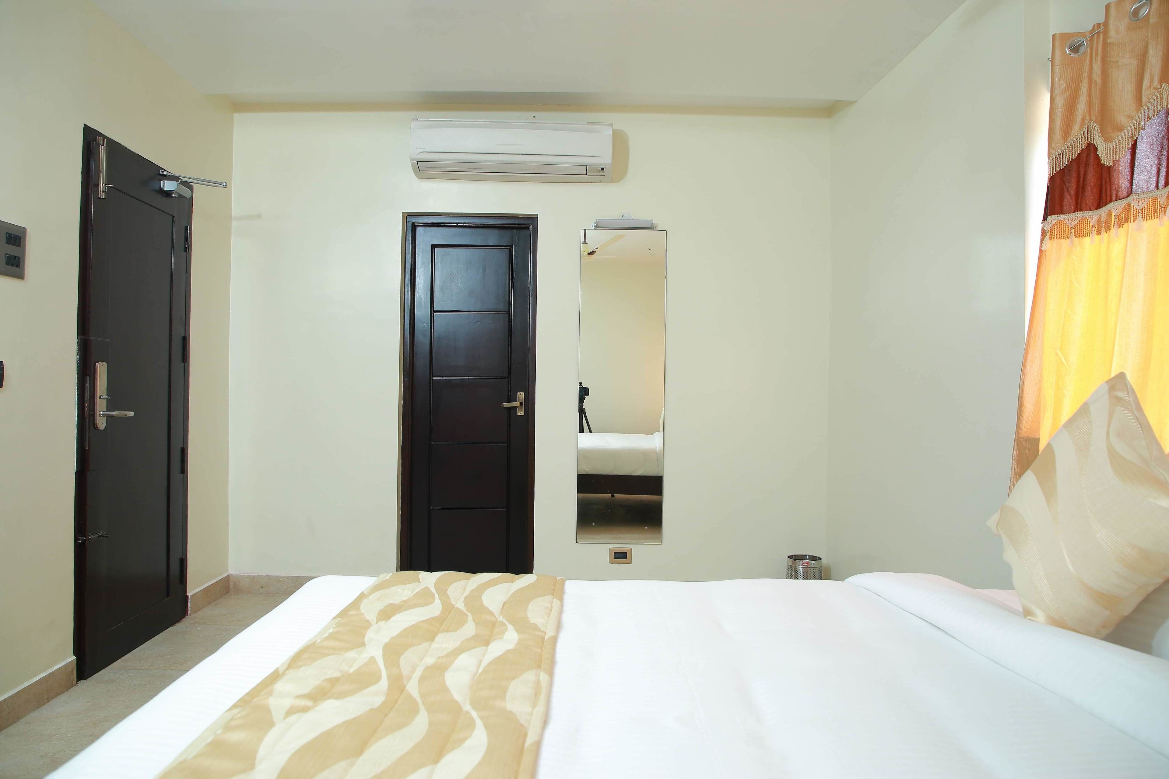 A hotel room with a bed, a door, a mirror, and an air conditioning unit.