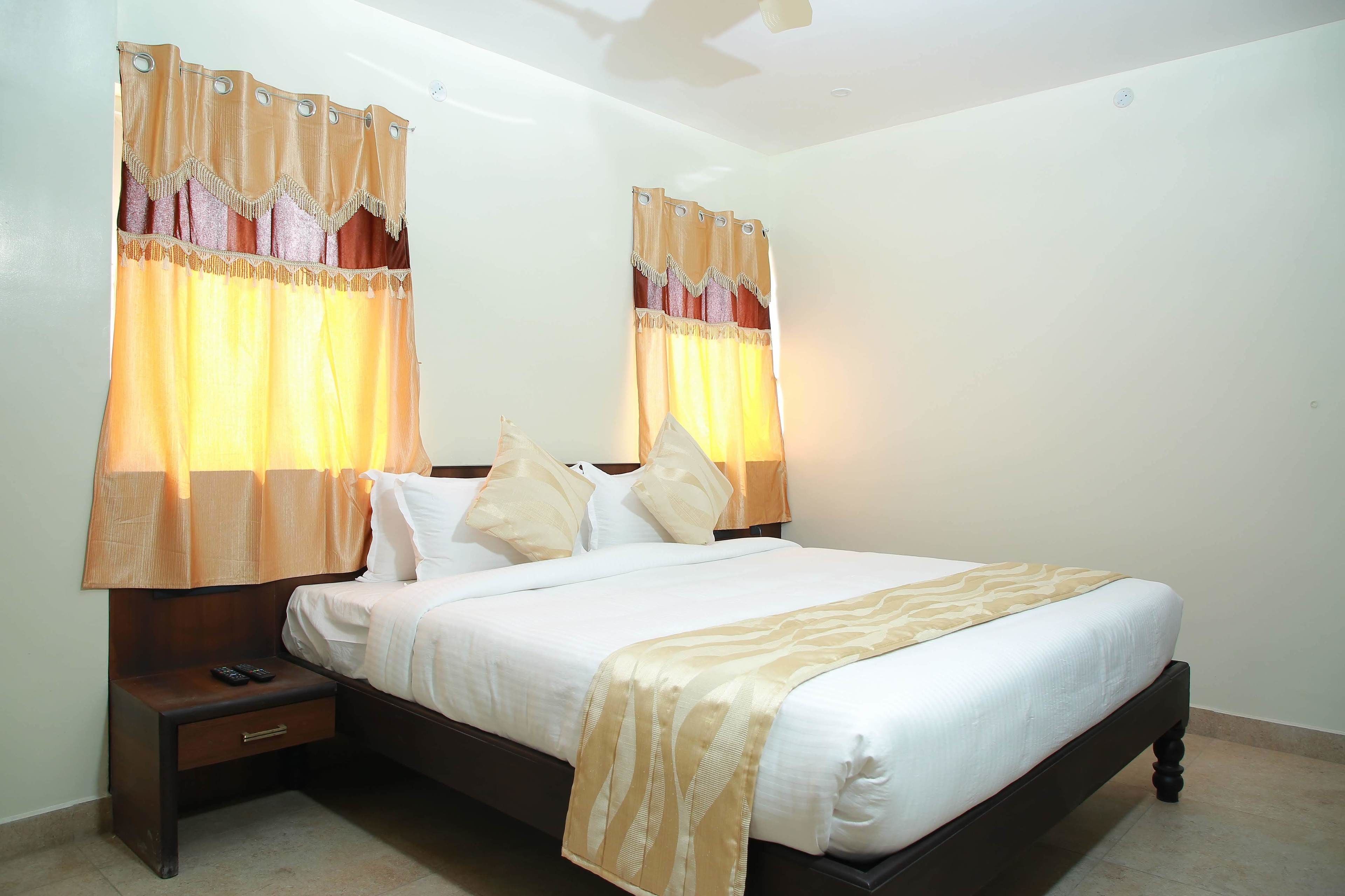A hotel room with a bed, nightstand, and curtains.
