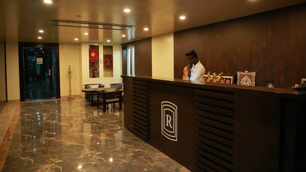 Een hotel receptie met een gepolijste marmeren vloer, een receptiebalie met een logo en een zithoek met tafels en stoelen.