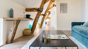 A cozy living room with exposed wooden beams, a black coffee table with decorative items, and a blue sofa. - Maison Deveney Mars (Puligny-Montrachet)
