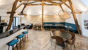 A rustic interior with exposed wooden beams, a stone wall, a herringbone floor, a bar area, and a seating arrangement. - Maison Deveney Mars (Puligny-Montrachet)