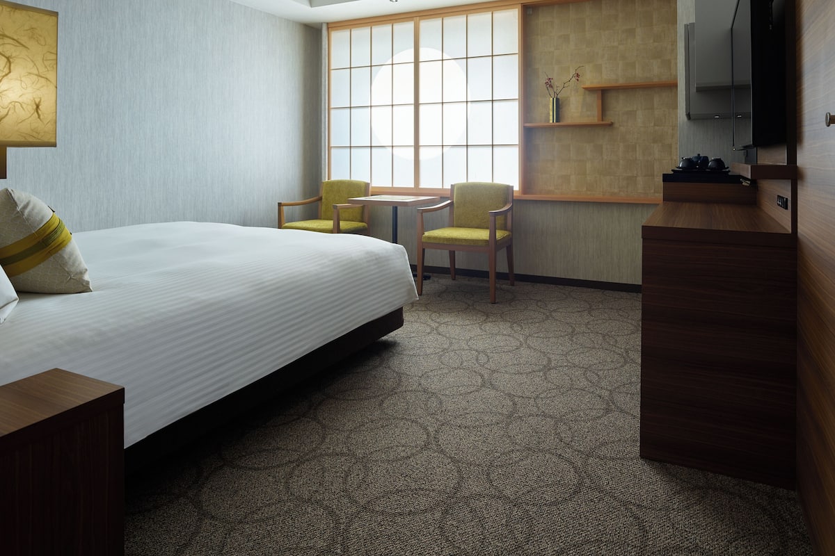 A hotel room with a bed, two chairs, a small table, a TV, and a window with a view.