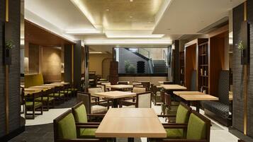 Interior de restaurante moderno con varias mesas y sillas tapizadas en verde.