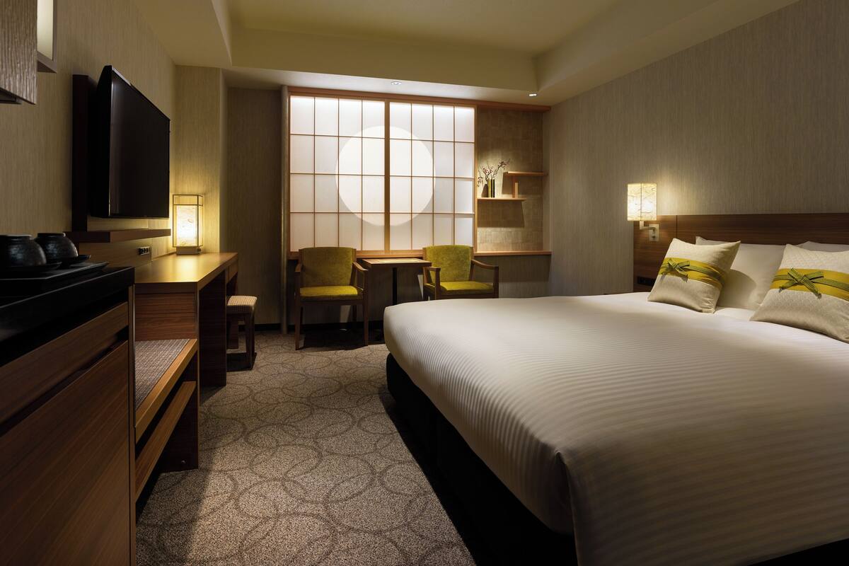A hotel room with a bed, a desk, a chair, a television, and a window.