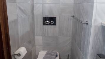 Un baño pequeño y moderno con inodoro, una toalla, un cesto de basura y una zona de ducha.