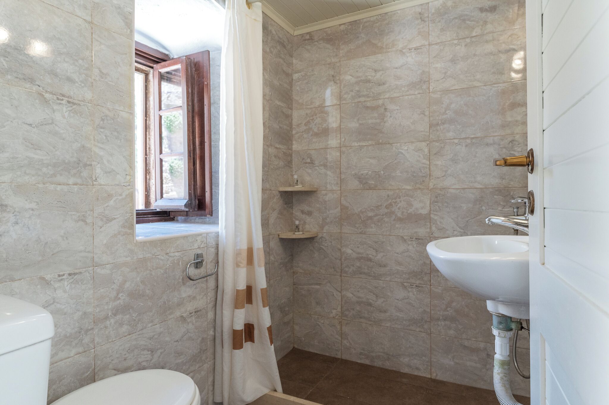 Une salle de bain comprenant des toilettes, une douche avec un rideau, un lavabo et une fenêtre donnant sur un paysage agréable.