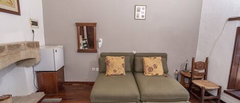A cozy room with a green sofa, a wooden chair, a small table, and a white appliance.