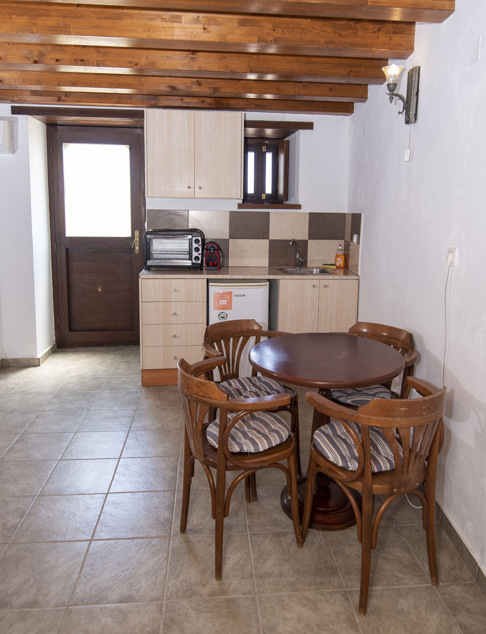 Une cuisine avec des meubles de rangement en bois, un four à micro-ondes encastré, un grille-pain et un évier. On y trouve également une table à manger avec quatre chaises.
