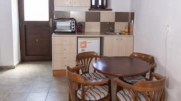 Une cuisine avec des meubles de rangement en bois, un four à micro-ondes encastré, un grille-pain et un évier. On y trouve également une table à manger avec quatre chaises.