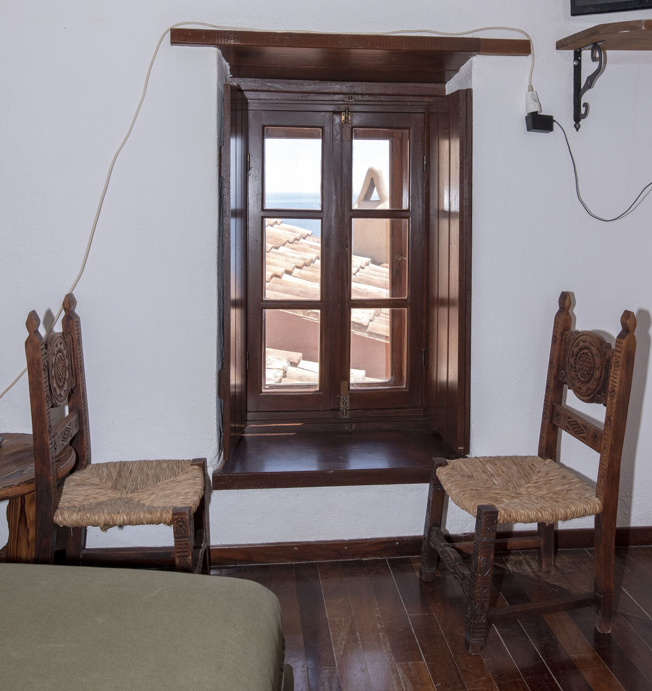 A room with a wooden window, two wooden chairs, and a bed.