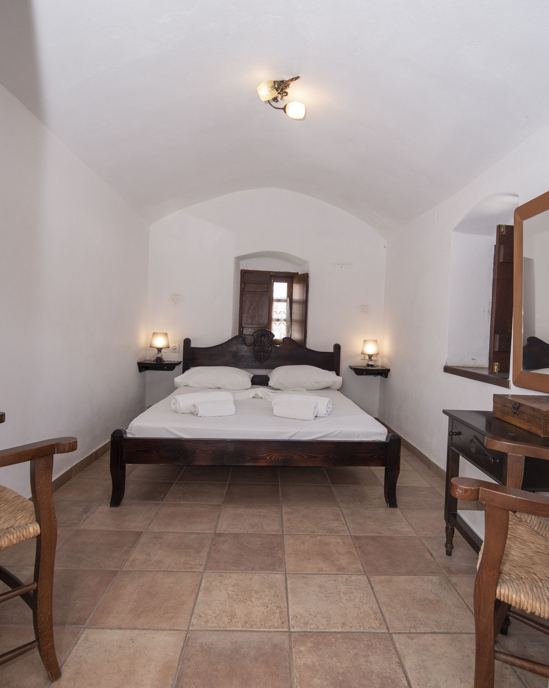 A bedroom with a wooden bed, two bedside tables with lamps, a large mirror, and a door with a window.