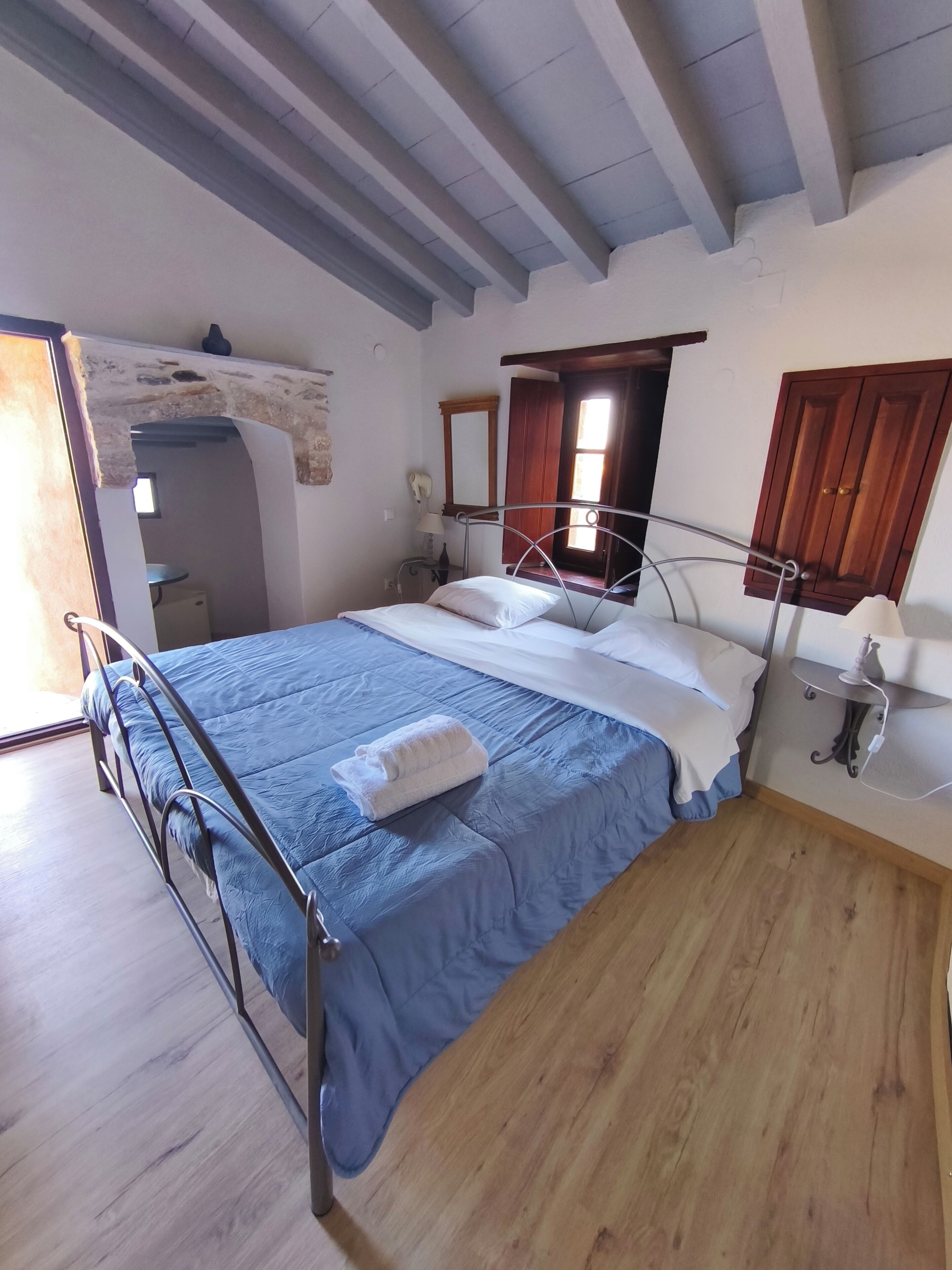 A bedroom with a bed, a wooden floor, a stone wall, a window, and a door.