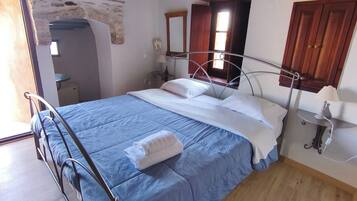 Un dormitorio con cama, piso de madera, pared de piedra, ventana y puerta.