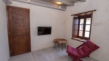 Una habitación con puerta de madera, un televisor de pantalla plana montado en la pared, una pequeña mesa redonda con un control remoto y una silla roja.