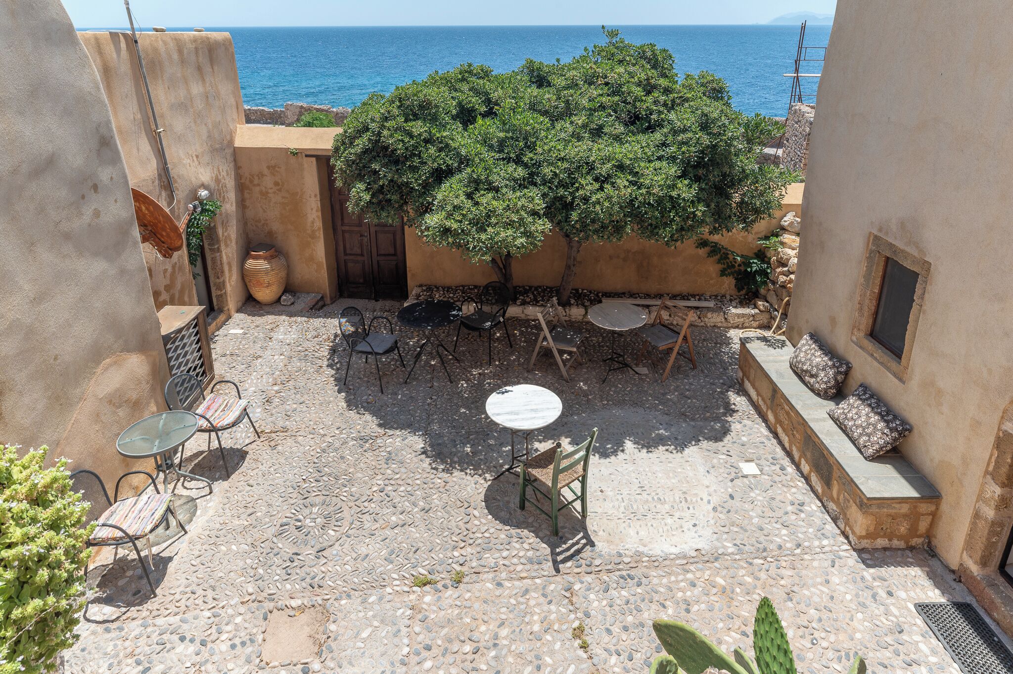 An outdoor patio with stone flooring, a tree, and a view of the sea.