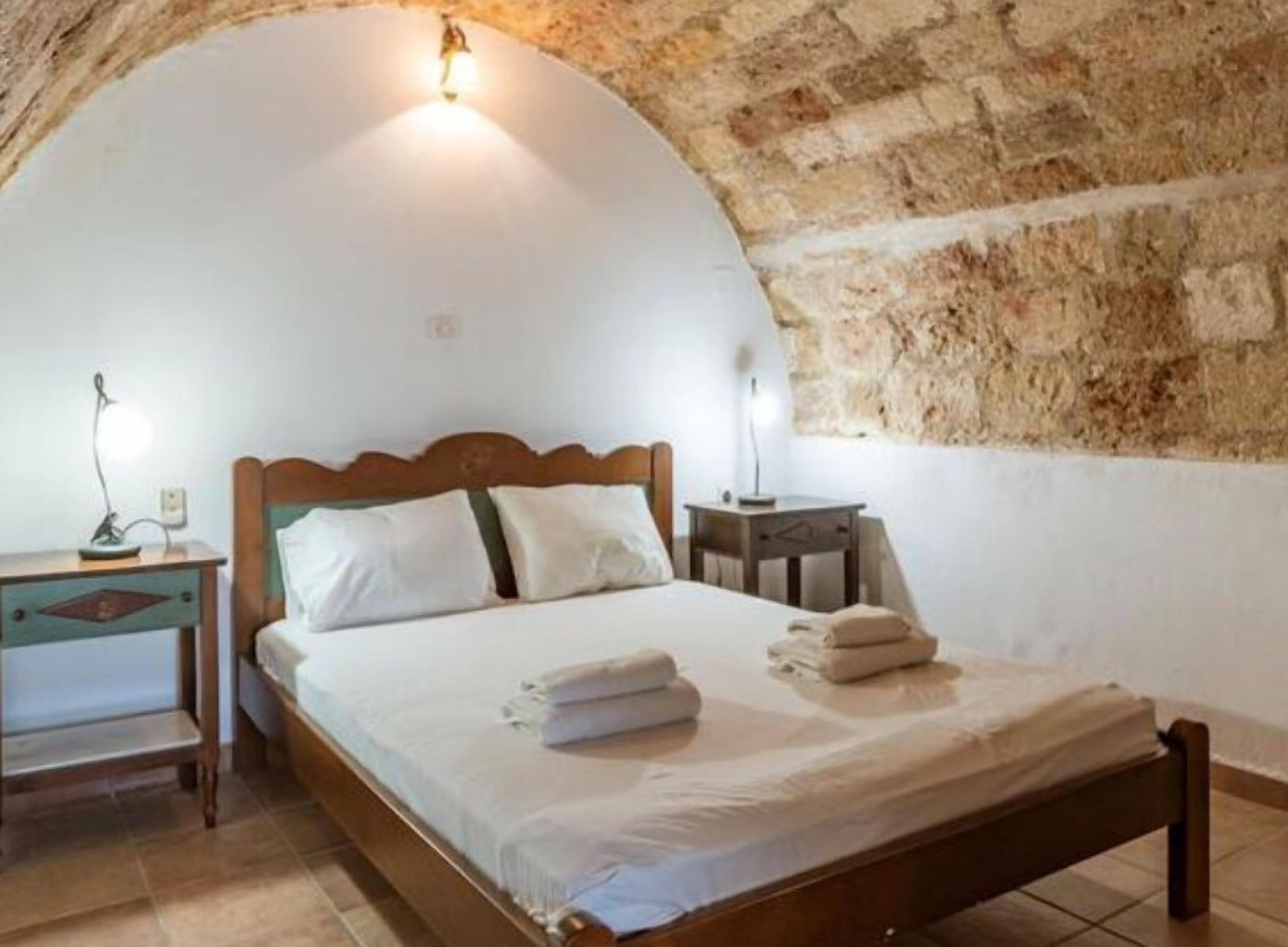 A bedroom with a wooden bed, white bedding, a nightstand, and a lamp.